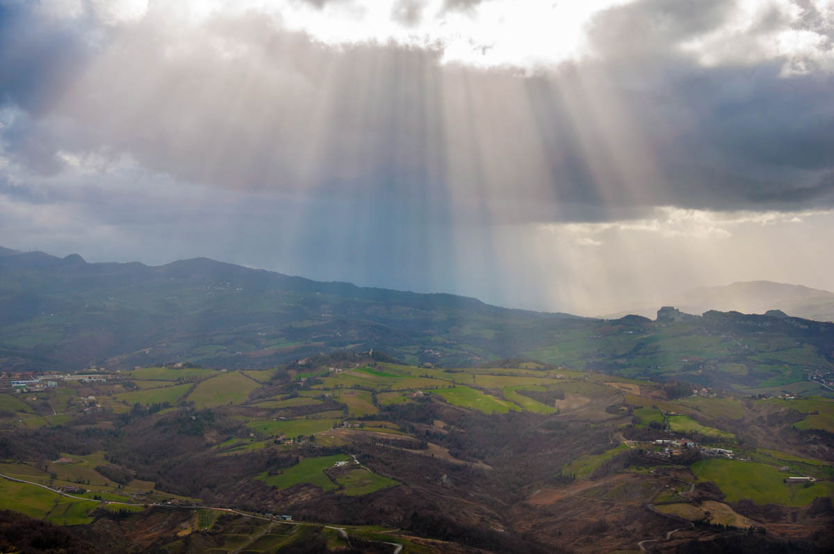 The sun coming through the clouds above the green hills that surround San Marino - rossiwrites.com