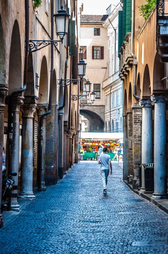 A boy in white walking down a cobbled street towards the daily market on Piazza delle Erbe - Padua, Italy - rossiwrites.com