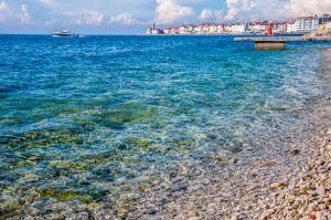 The crystal clear water of the Adriatic Sea with Punta Madonna in the background - Piran, Slovenia - www.rossiwrites.com