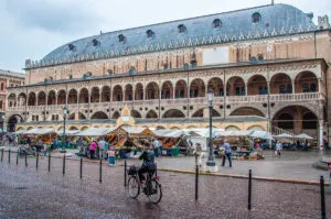 A lady on a bike passing in front of Palazzo della Ragione and the market at Piazza delle Erbe, Padua, Veneto, Italy - rossiwrites.com