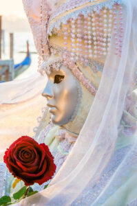 A beautiful mask holding a rose in front of the St. Mark's Basin - Venice, Italy - rossiwrites.com