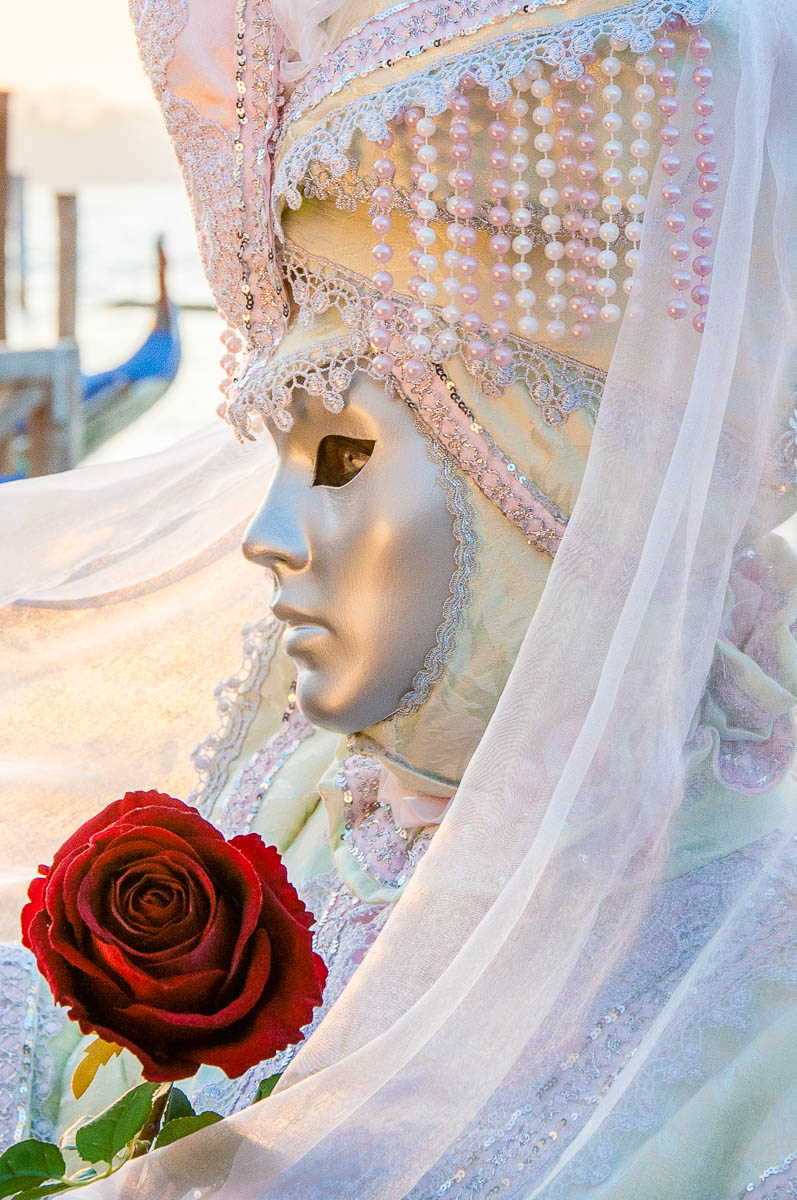 A beautiful mask holding a rose in front of the St. Mark's Basin - Venice, Italy - rossiwrites.com