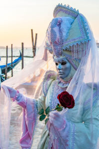 A beautiful mask holding a rose in front of the St. Mark's Basin - Venice, Italy - rossiwrites.com