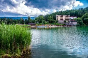 View of Lake Lavarone with a hotel and sandy beach in the distance - Trentino, Italy - rossiwrites.com