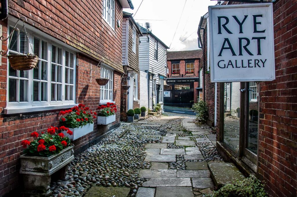 A small street with red flowers and a sign for Rye Art Gallery - Rye, England - rossiwrites.com