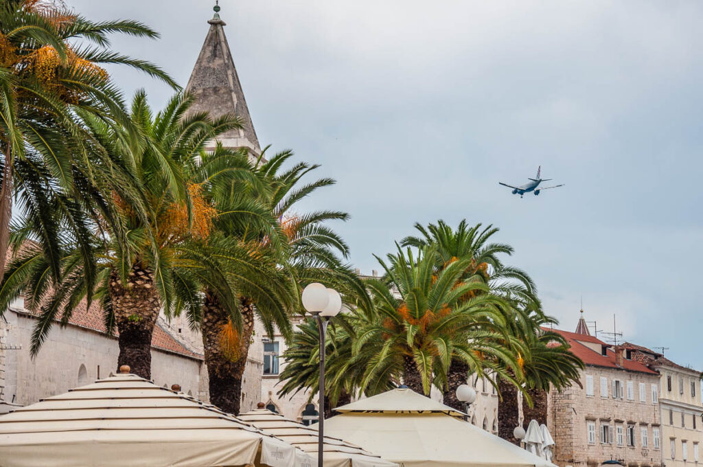 Plane flying over the palm-fringed promenade - Trogir, Croatia - rossiwrites.com