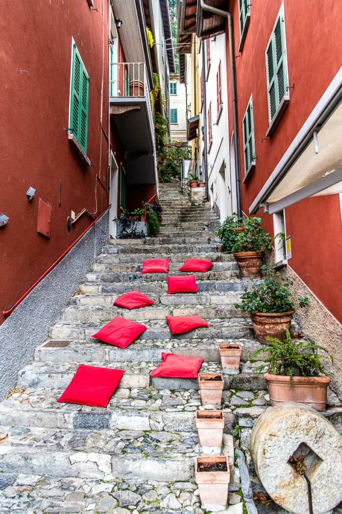 Steep side street with red cushions on the steps in the town of Varenna - Lake Como, Italy - rossiwrites.com