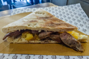 A slice of torta al testo with local sausage and potatoes as served in Testone - Perugia, Italy - rossiwrites.com