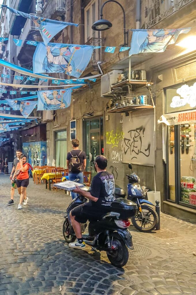 Scene of Spaccanapoli with a moped driver holding a pizza - Naples, Italy - rossiwrites.com